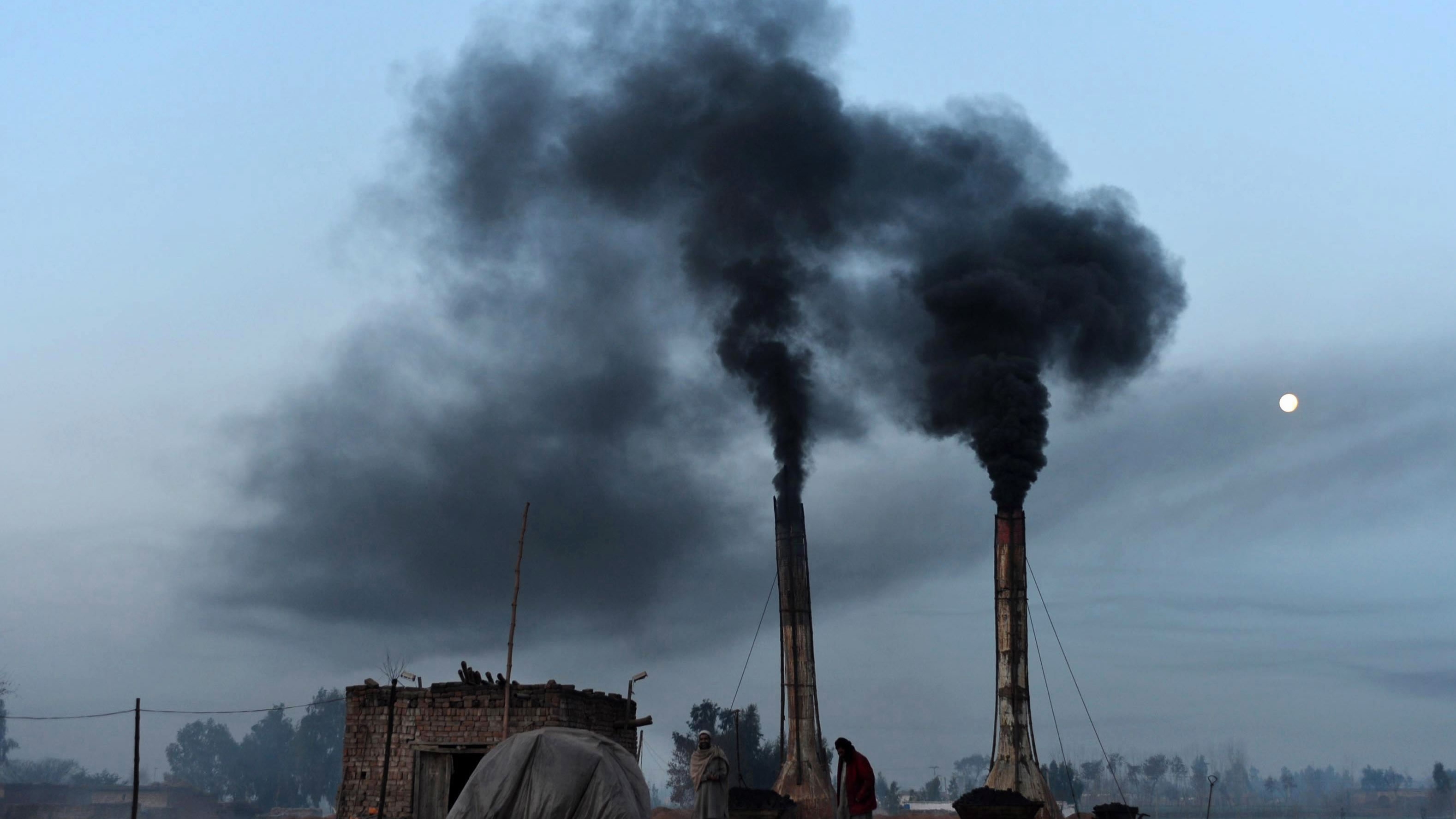 Brick kiln chimneys emitting thick black smoke at dusk